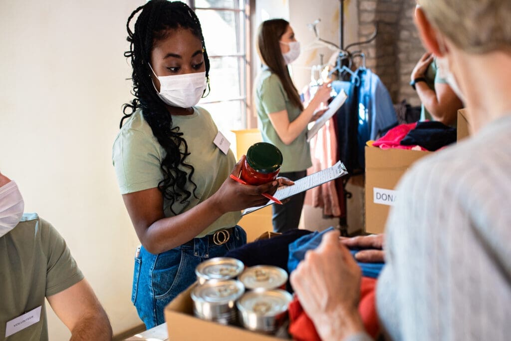 An instructor wearing a face mask demonstrates or teaches a workshop activity to a group of participants in an indoor classroom or community space.