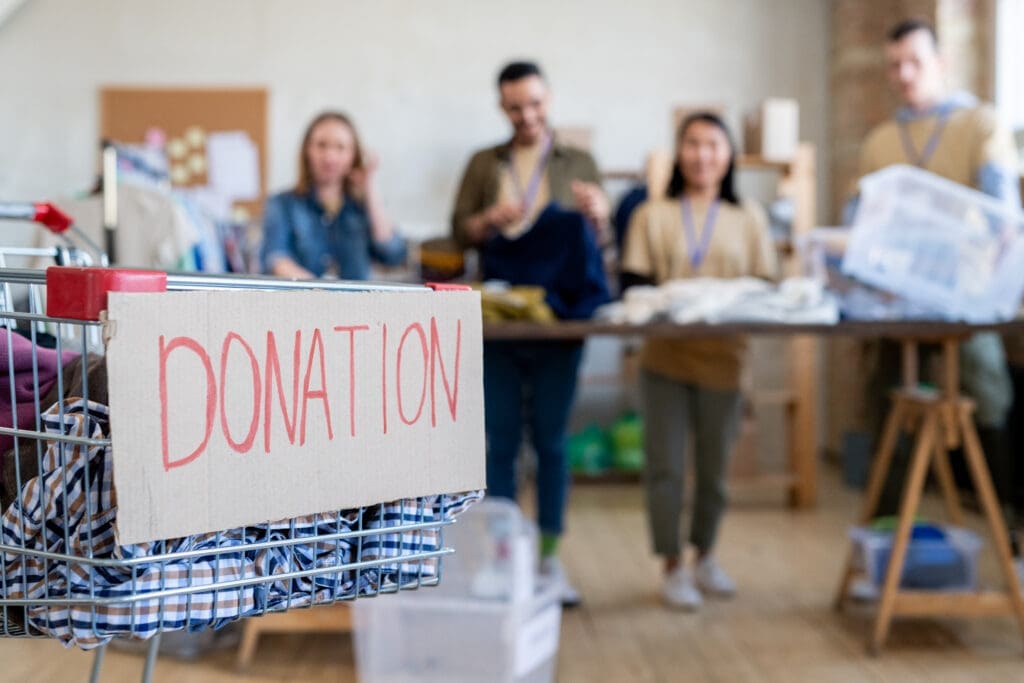 A charity donation drive with volunteers gathered in a community space, featuring a donation basket with a handwritten sign in the foreground.