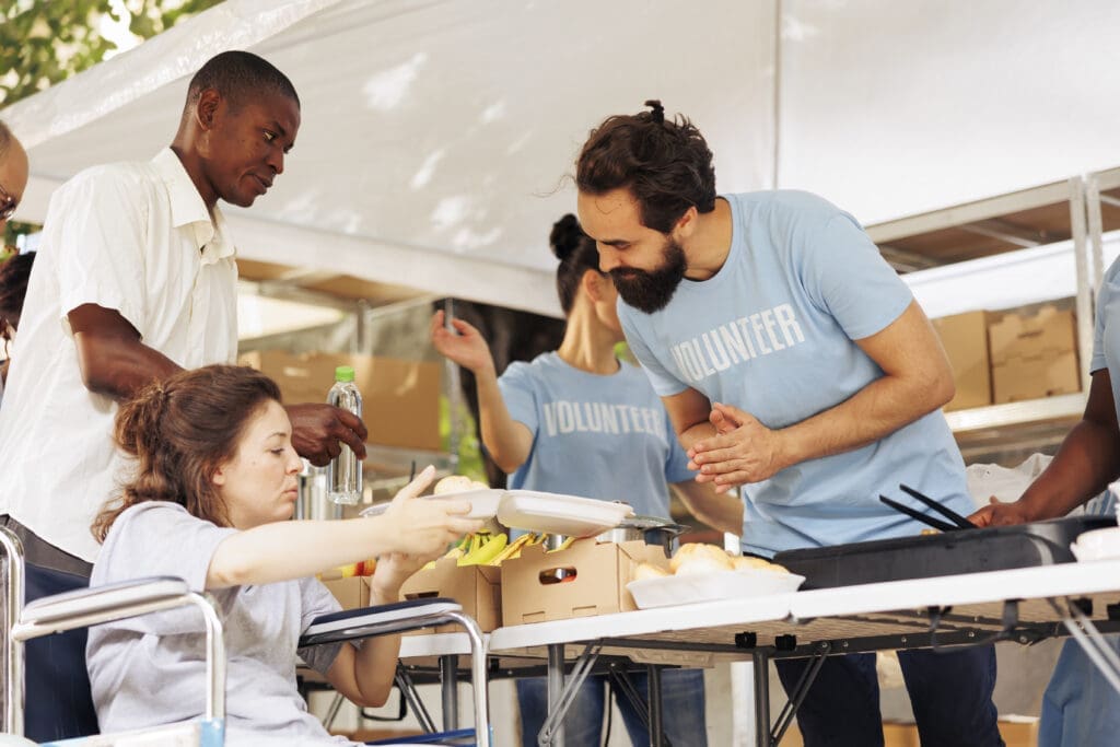 An instructor demonstrates woodworking techniques to a young student at a workshop table while other participants observe the hands-on lesson.